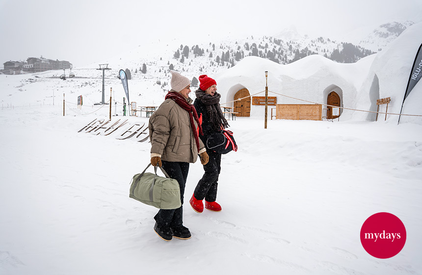 Zwei Frauen stehen mit Gepäck vor Iglus im Schnee