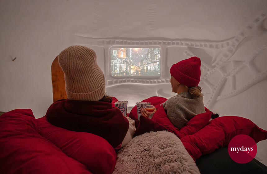 Zwei Frauen liegen im Iglu im Bett und schauen einen Film