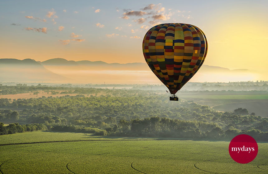 Ballonfahrt über grüner Landschaft mit Bergen in Hintergrund