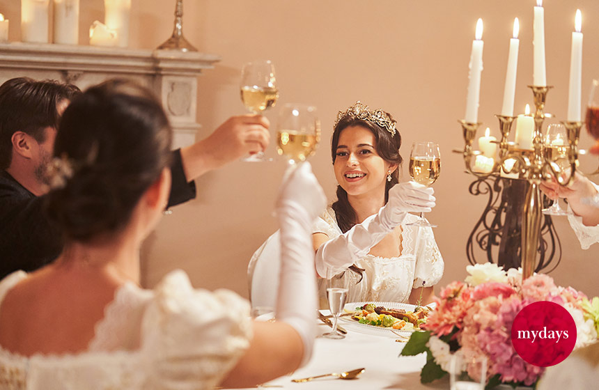Adlig gekleidete Menschen stoßen am Tisch miteinander an