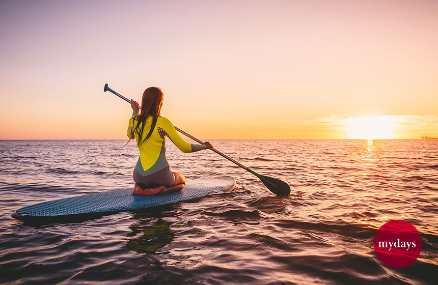 Eine Frau sitzt auf einem SUP und schaut sich den Sonnenuntergang an