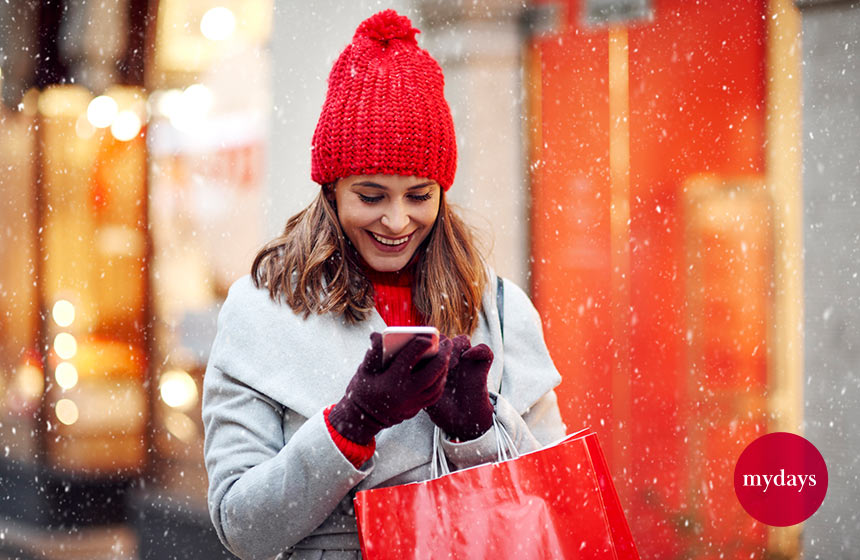 Eine Frau steht mit Einkaufstasche im Schnee und guckt auf ihr Handy