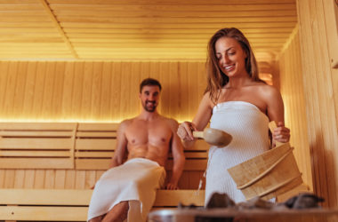 Frau gießt Sauna Auf mit Mann im Hintergrund
