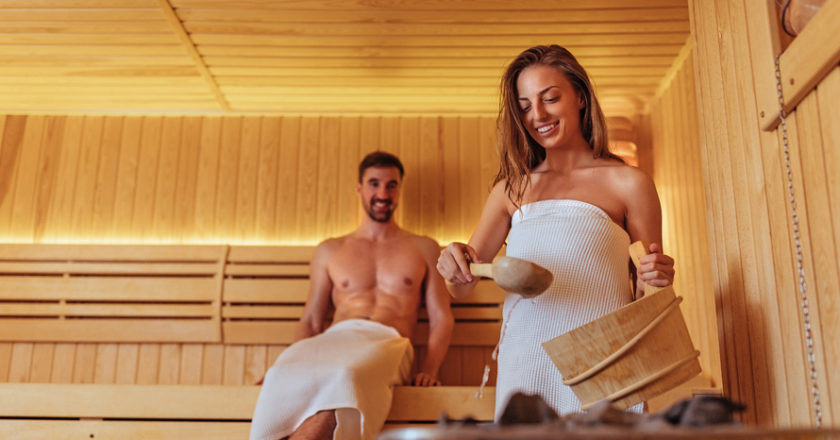 Frau gießt Sauna Auf mit Mann im Hintergrund