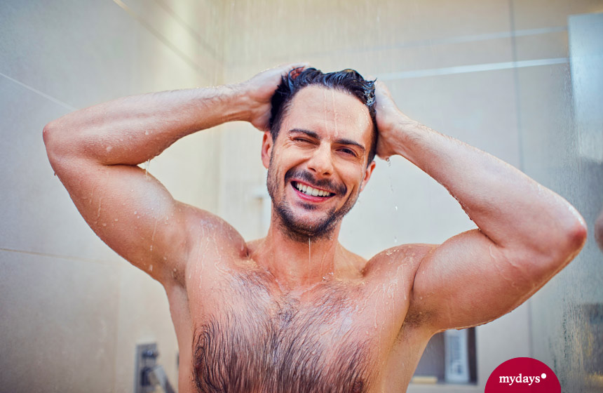 Mann wäscht sich die haare unter einer Dusche und grinst