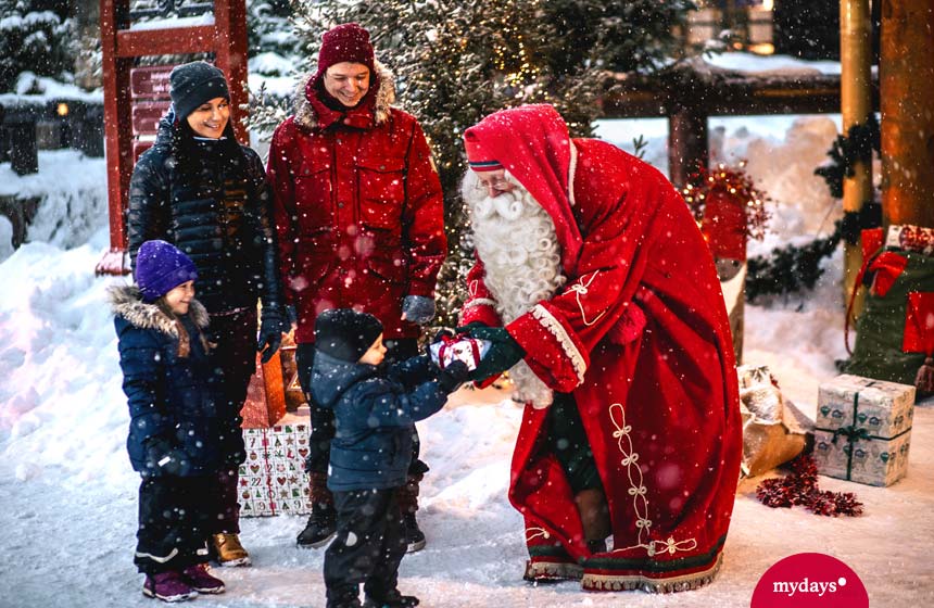 Weihnachtsmann übergibt Geschenk an kleines Kind mit Eltern und Schwester im Hintergrund