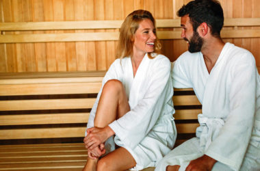 Paar sitzt mit Bademänteln in der Sauna und lächelt sich an