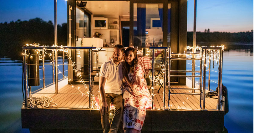 Paar sitzt auf einem Hausboot mit Lichterketten in der Dämmerung