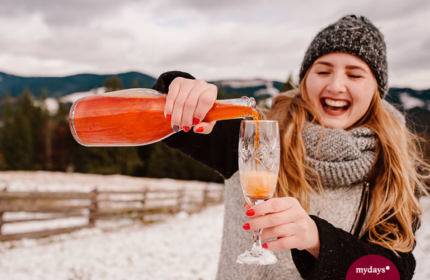 Mädchen im Schnee mit Rollkragenpullover und Mützi trinkt Aperol