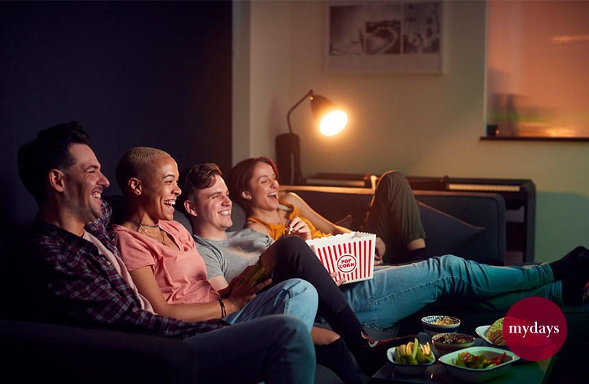 Gruppe von fröhlichen Freunden essen Popcorn, sitzen auf dem Sofa zu Hause, schauen Fernsehen und entspannen zusammen