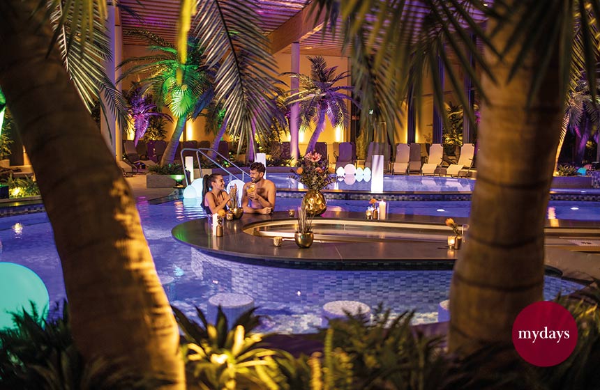 Paar bei stimmungsvoller Beleuchtung mit Cocktails in der Hand an der Poolbar der Havel Therme